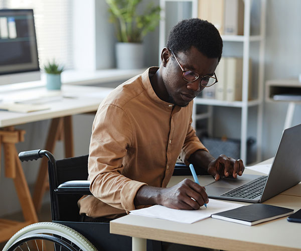 disabled black man works at desk with open laptop